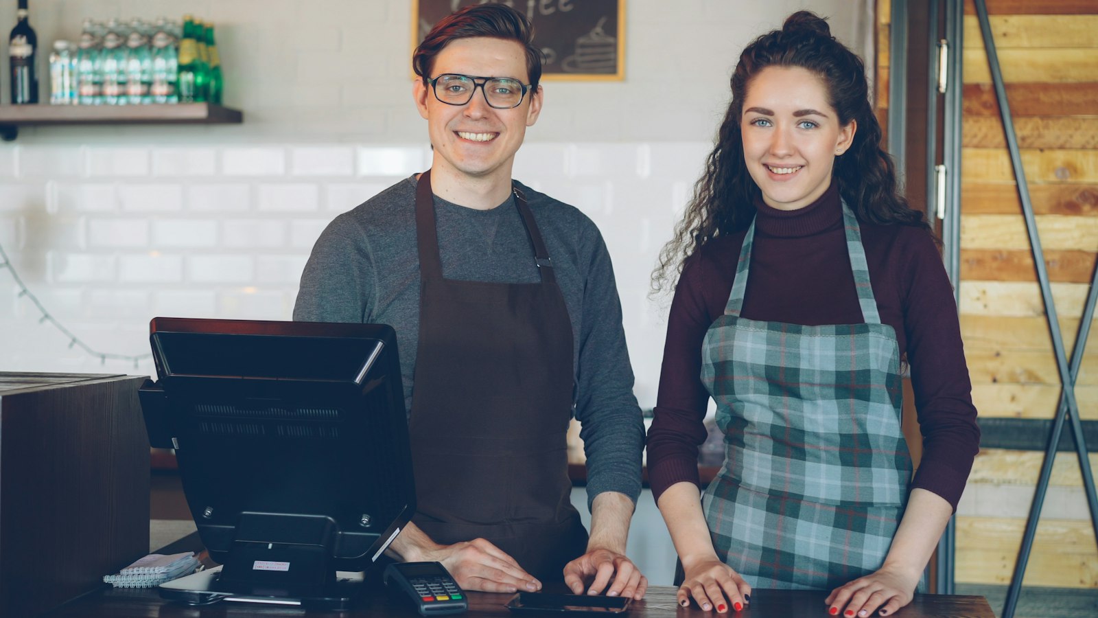 Dois donos de cafeteria sorrindo atrás do balcão, ao lado do sistema de ponto de venda