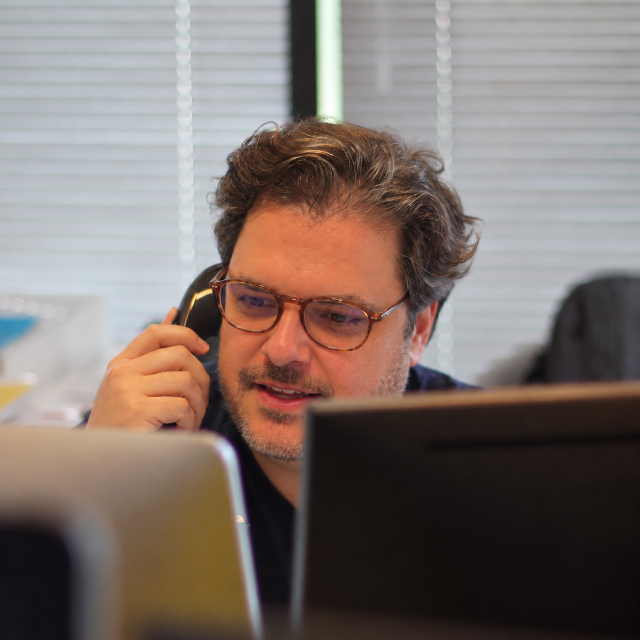 Atendente de suporte sorrindo enquanto fala ao telefone, em frente ao computador